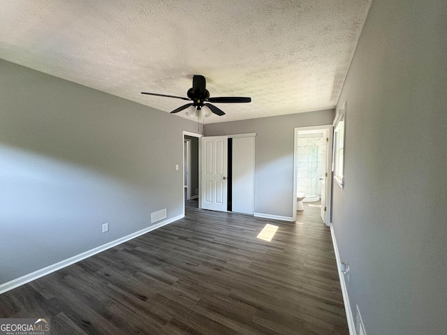 unfurnished bedroom featuring a textured ceiling, ensuite bathroom, ceiling fan, and dark hardwood / wood-style floors