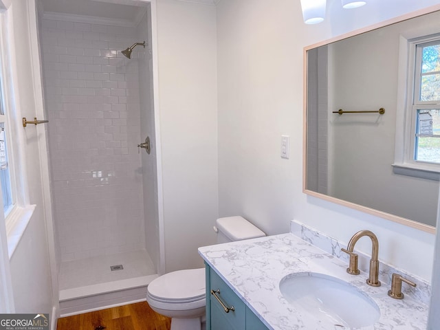 bathroom with toilet, a tile shower, hardwood / wood-style floors, and vanity