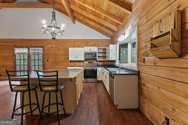 kitchen featuring white cabinetry, hanging light fixtures, stainless steel appliances, a kitchen island, and wood walls