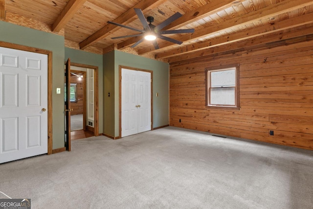 unfurnished bedroom with ceiling fan, wooden walls, carpet floors, wooden ceiling, and beamed ceiling