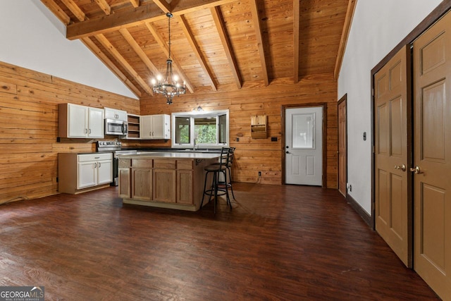 kitchen with a kitchen island, appliances with stainless steel finishes, wooden walls, white cabinetry, and hanging light fixtures