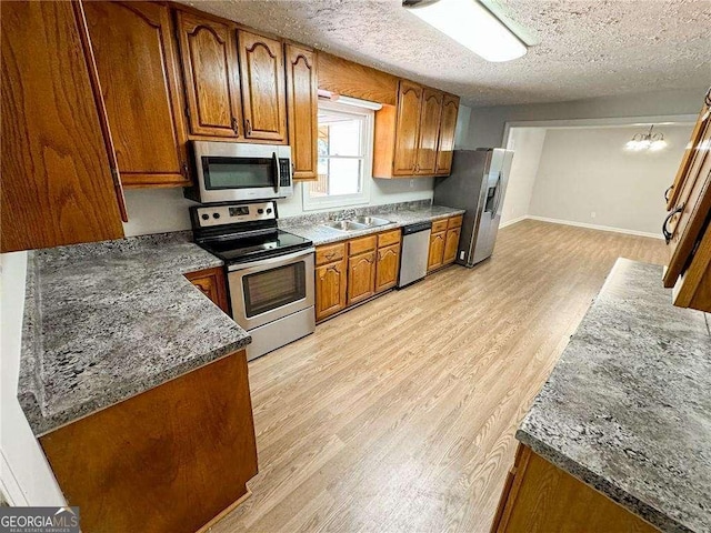 kitchen with sink, light hardwood / wood-style flooring, a textured ceiling, appliances with stainless steel finishes, and a notable chandelier