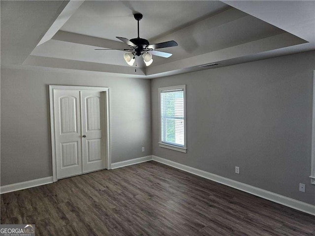 interior space with a tray ceiling, ceiling fan, a closet, and dark wood-type flooring