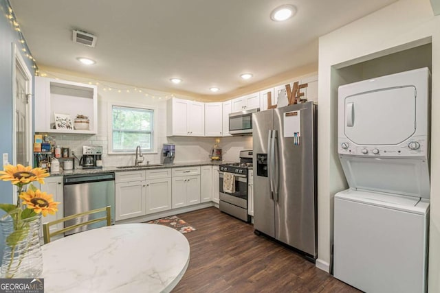 kitchen featuring sink, stacked washing maching and dryer, light stone counters, white cabinets, and appliances with stainless steel finishes