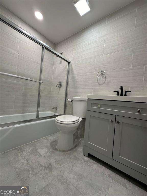 full bathroom featuring vanity, enclosed tub / shower combo, tile walls, and toilet