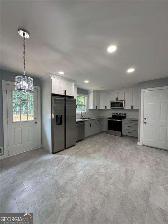 kitchen featuring stainless steel appliances, sink, a chandelier, white cabinetry, and hanging light fixtures