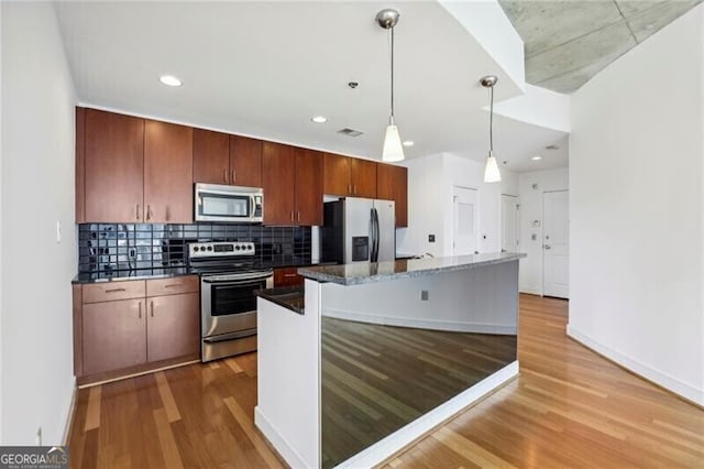 kitchen with decorative backsplash, stainless steel appliances, light hardwood / wood-style flooring, a kitchen island, and hanging light fixtures