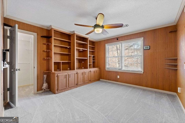 interior space featuring wood walls, a textured ceiling, ceiling fan, and ornamental molding