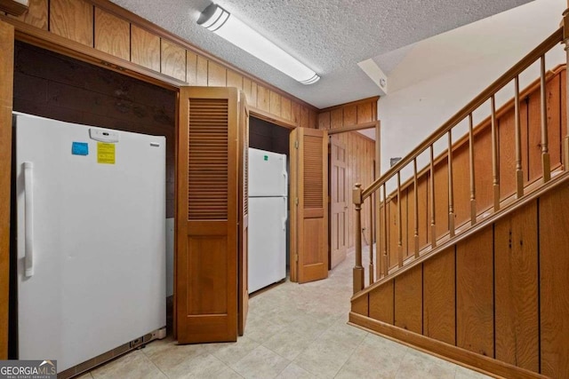 kitchen featuring a textured ceiling, white fridge, and wooden walls