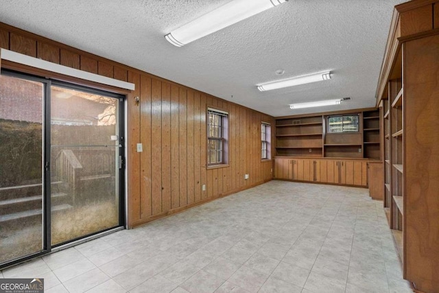 unfurnished room with wood walls, a textured ceiling, built in features, and a wealth of natural light