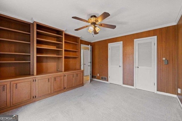 unfurnished living room with wooden walls, ceiling fan, crown molding, and light colored carpet