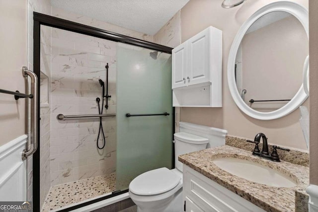 bathroom with a textured ceiling, vanity, a shower with shower door, and toilet