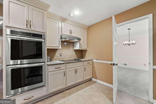 kitchen with light stone counters, a chandelier, black electric stovetop, backsplash, and double oven