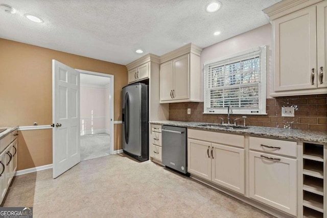 kitchen with light stone countertops, decorative backsplash, appliances with stainless steel finishes, cream cabinetry, and sink