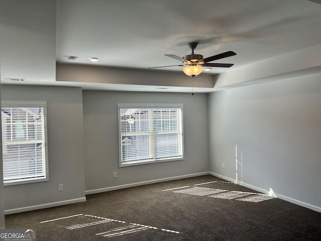 empty room featuring dark colored carpet, ceiling fan, and a tray ceiling