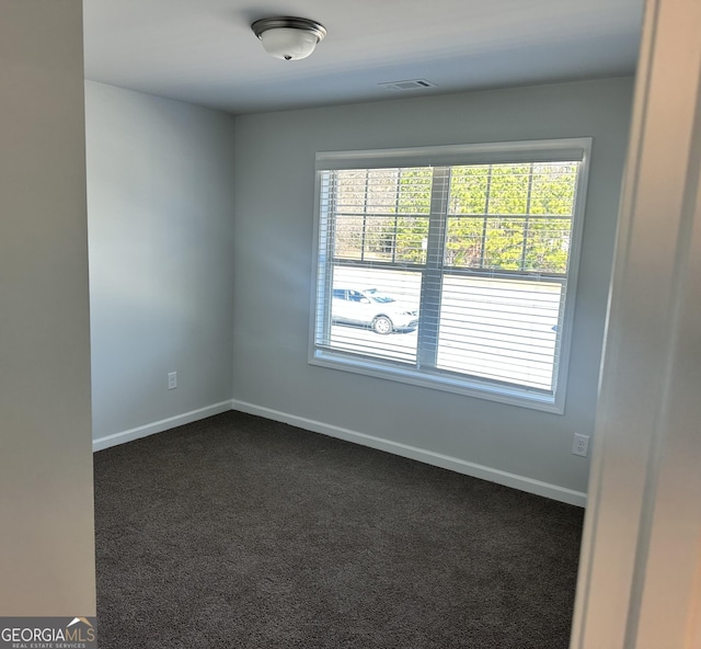 spare room with dark colored carpet and a wealth of natural light