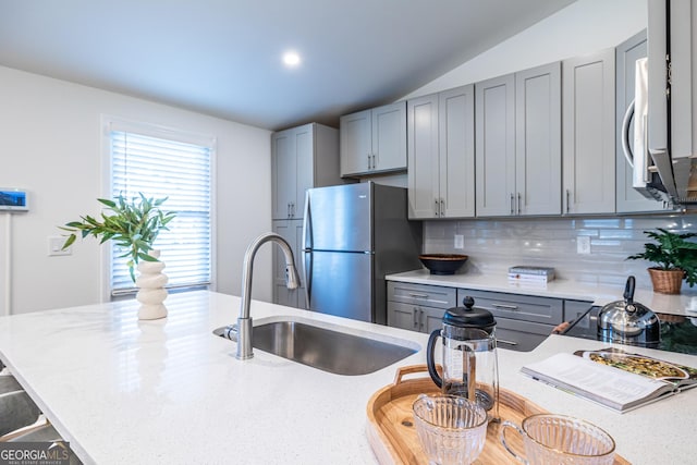 kitchen featuring stainless steel appliances, tasteful backsplash, gray cabinets, a sink, and a kitchen bar