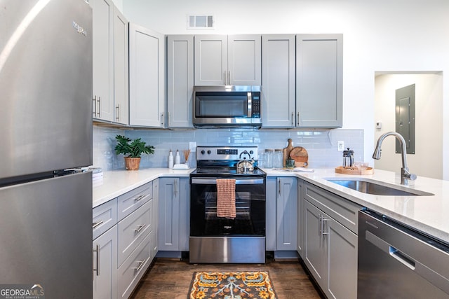 kitchen featuring dark wood-style floors, stainless steel appliances, tasteful backsplash, gray cabinets, and a sink