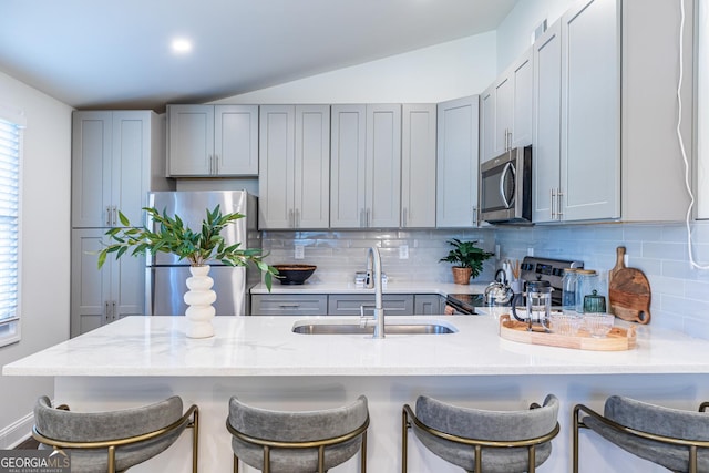 kitchen featuring gray cabinetry, stainless steel appliances, a peninsula, a sink, and decorative backsplash