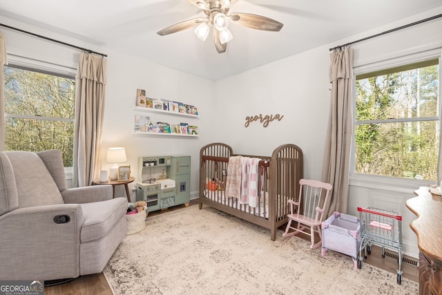 bedroom with ceiling fan, light hardwood / wood-style floors, and a crib