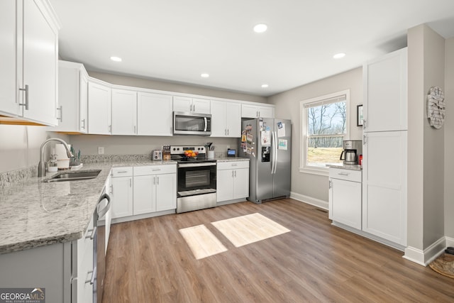 kitchen featuring light stone countertops, stainless steel appliances, white cabinetry, and sink