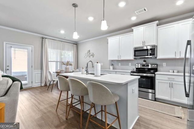 kitchen featuring pendant lighting, white cabinets, stainless steel appliances, and a kitchen island with sink