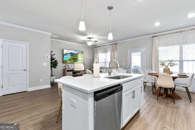 kitchen featuring stainless steel dishwasher, a kitchen island with sink, sink, white cabinetry, and hanging light fixtures