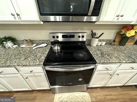 kitchen with white cabinets, light stone counters, stainless steel appliances, and hardwood / wood-style flooring