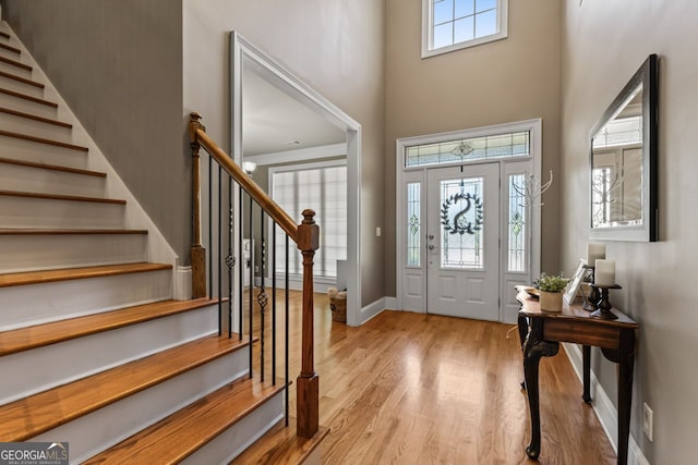 foyer entrance featuring stairs, light wood finished floors, a towering ceiling, and baseboards