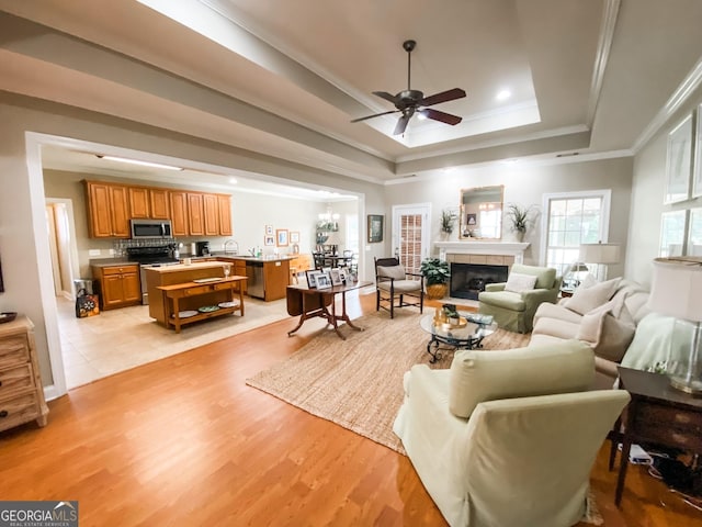 living room with ceiling fan, light wood-type flooring, a tray ceiling, a tiled fireplace, and ornamental molding