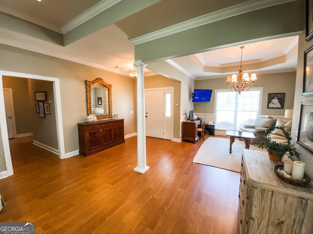 living room with decorative columns, a raised ceiling, crown molding, light hardwood / wood-style flooring, and a chandelier