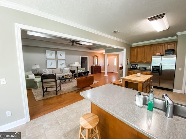 kitchen with ceiling fan, wood counters, stainless steel fridge with ice dispenser, crown molding, and a textured ceiling