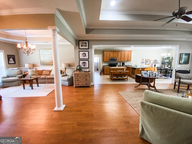 living room with a tray ceiling, ornate columns, light hardwood / wood-style floors, and ceiling fan with notable chandelier