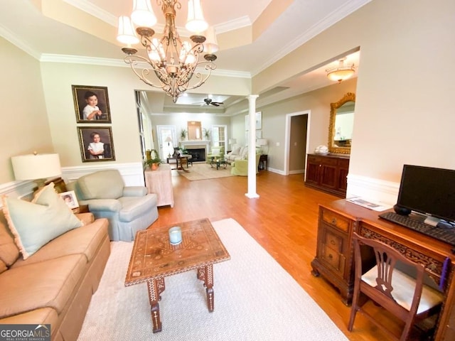 living room featuring ceiling fan with notable chandelier, light hardwood / wood-style floors, a raised ceiling, and decorative columns