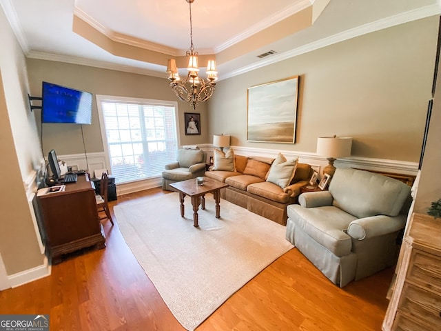 living room featuring a chandelier, wood-type flooring, ornamental molding, and a tray ceiling