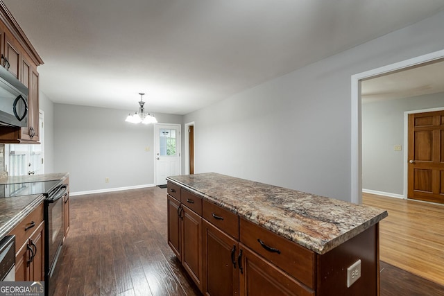 kitchen featuring dark hardwood / wood-style flooring, decorative light fixtures, black / electric stove, a kitchen island, and an inviting chandelier