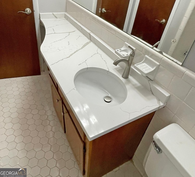 bathroom with toilet, tile walls, tile patterned flooring, and vanity