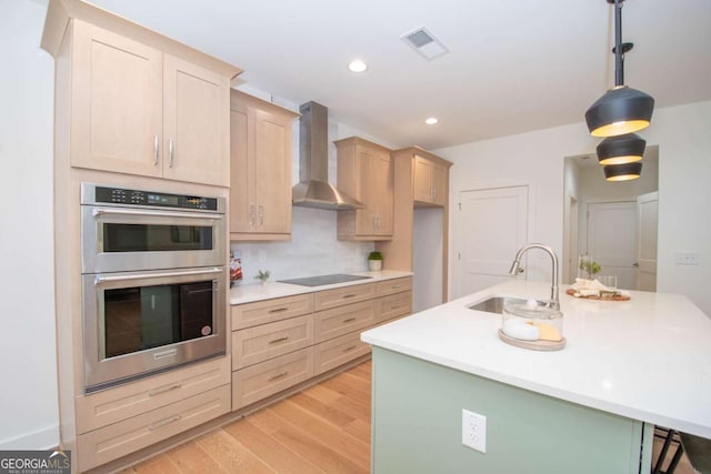 kitchen featuring sink, wall chimney exhaust hood, hanging light fixtures, double oven, and light brown cabinetry