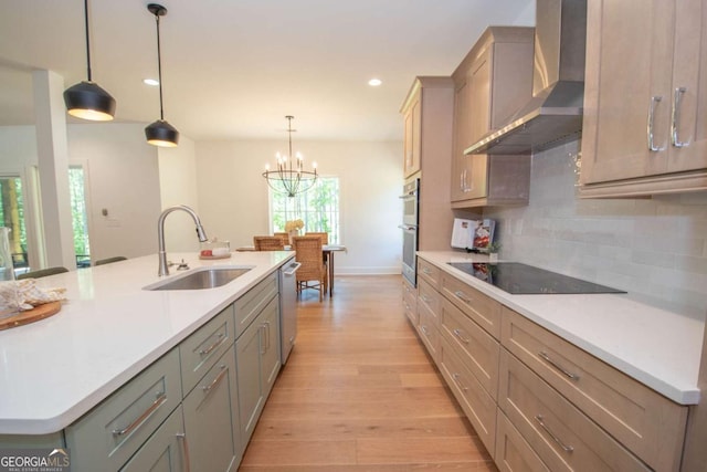 kitchen with a center island with sink, sink, wall chimney exhaust hood, appliances with stainless steel finishes, and decorative light fixtures