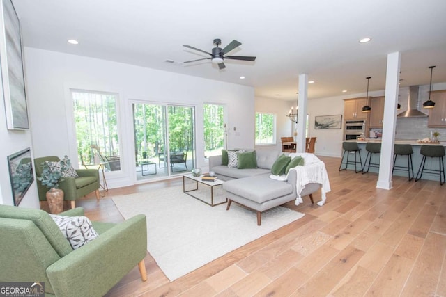 living room featuring ceiling fan with notable chandelier and light wood-type flooring