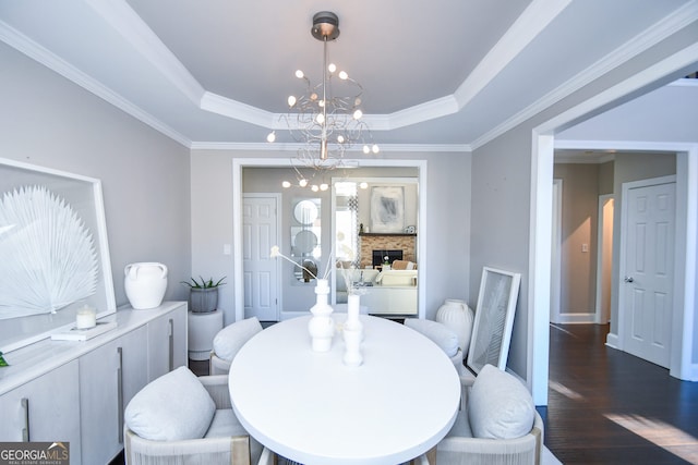 dining space featuring a chandelier, a tray ceiling, a stone fireplace, and dark hardwood / wood-style floors