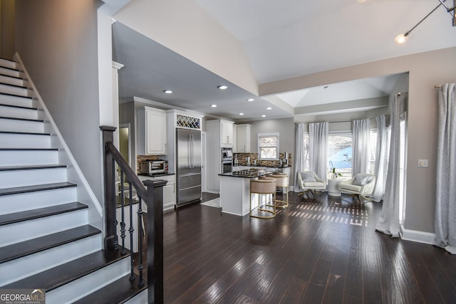 interior space with decorative backsplash, a kitchen breakfast bar, a kitchen island, white cabinetry, and lofted ceiling