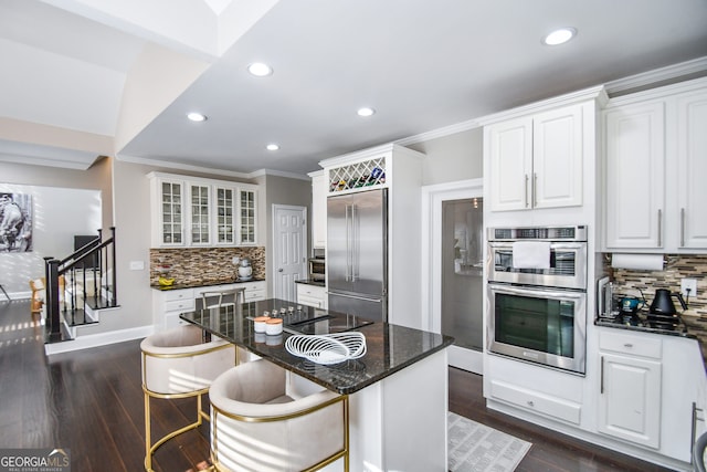 kitchen with a center island, dark stone counters, white cabinets, a kitchen breakfast bar, and appliances with stainless steel finishes