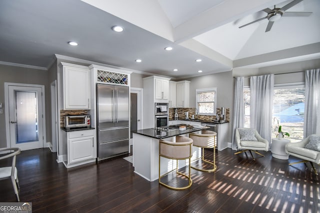 kitchen with white cabinetry, tasteful backsplash, a kitchen breakfast bar, vaulted ceiling, and appliances with stainless steel finishes