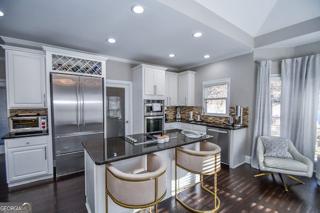 kitchen featuring decorative backsplash, stainless steel appliances, dark stone countertops, a center island, and white cabinetry