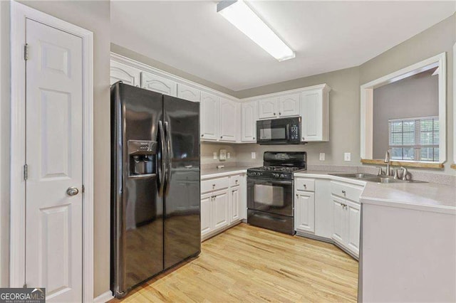 kitchen with white cabinetry, sink, black appliances, and light wood-type flooring