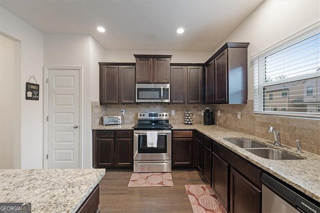 kitchen with sink, appliances with stainless steel finishes, dark hardwood / wood-style flooring, light stone counters, and dark brown cabinetry