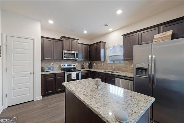 kitchen featuring appliances with stainless steel finishes, dark hardwood / wood-style flooring, a kitchen island, and light stone counters