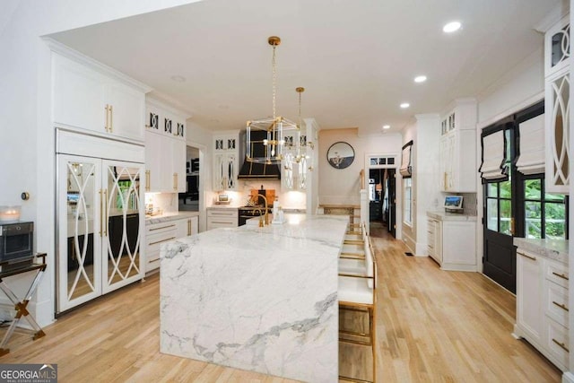 kitchen featuring a breakfast bar area, white cabinetry, a spacious island, light stone countertops, and paneled fridge