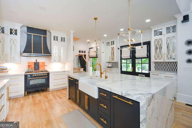 kitchen featuring pendant lighting, sink, a large island with sink, black appliances, and wall chimney exhaust hood